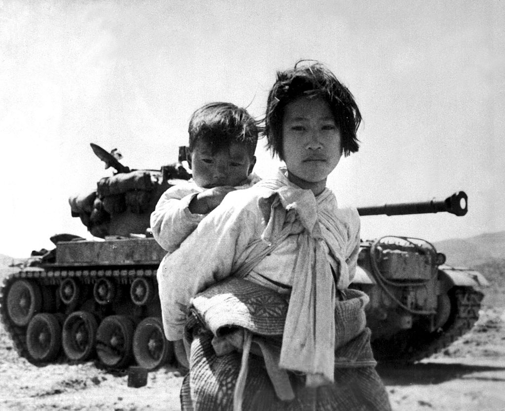 A war weary Korean girl walks by a stalled M-26 tank 