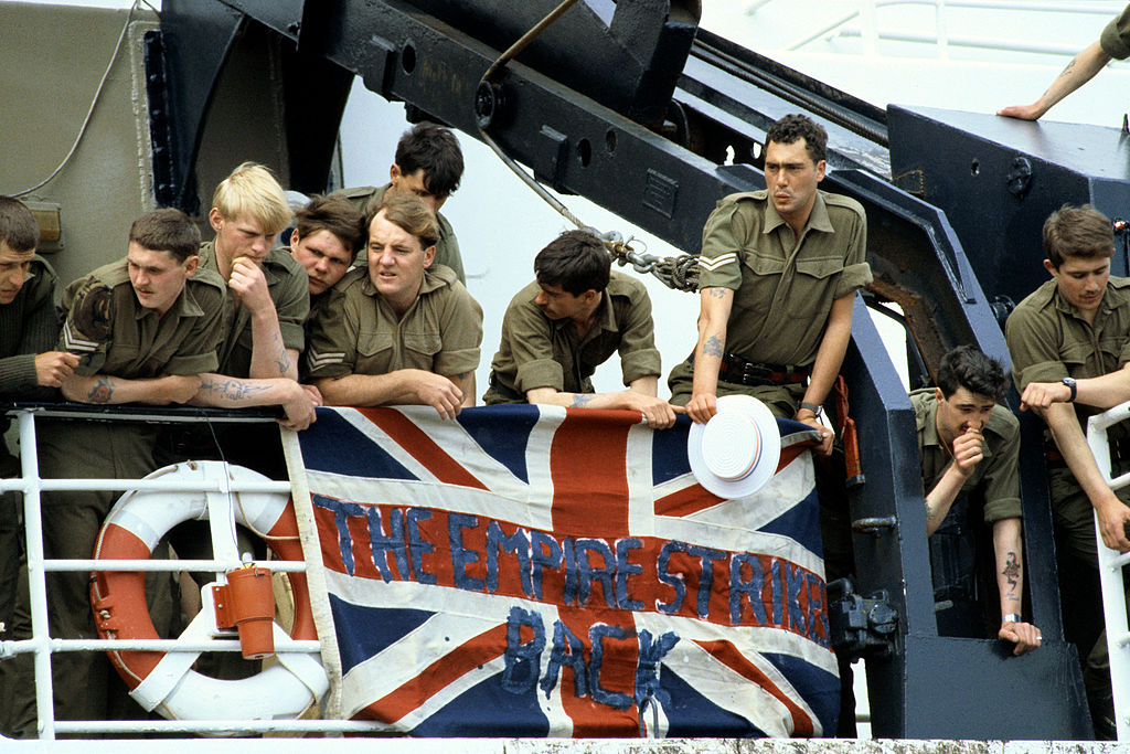Troops hold a British Union Jack over the ships railings, with the slogan which reads ' The Empire Strikes Back', as they stand on board the deck of the RMS Queen Elizabeth 2 