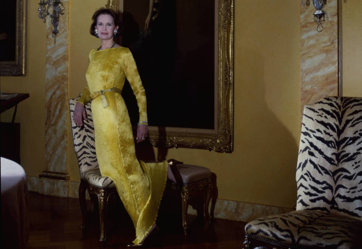 Fashion designer Gloria Vanderbilt wearing a pleated dress most likely by Fortuny and posing in front of a large portrait of her mother in her penthouse in Gracie Square in New York City.