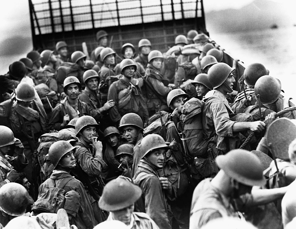 American troops helmeted and bearing fighting packs, ride an LCI