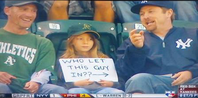 young oakland a's fan with a sign pointed at a yankees fan