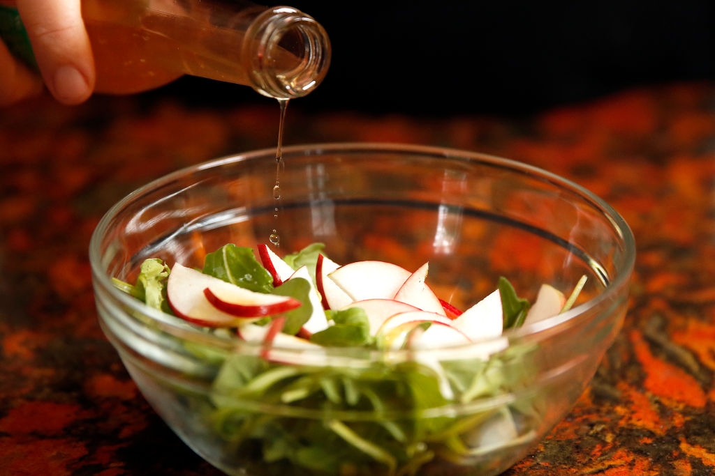 Dressing is poured from a bottle over a small salad.