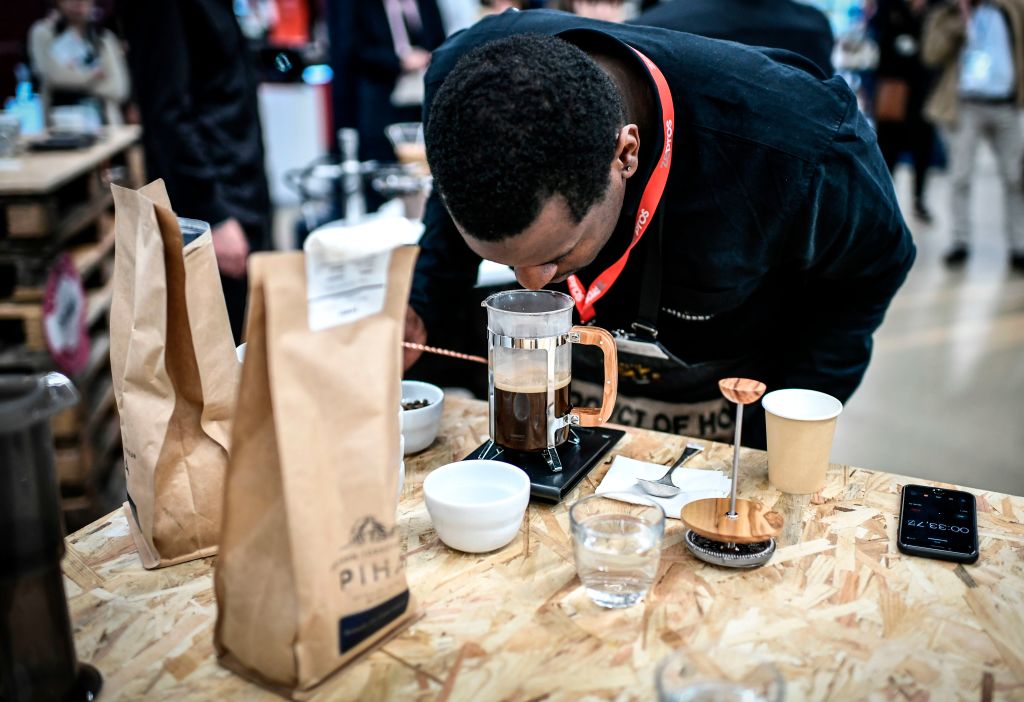 A man leans down to smell coffee brewing in a french press.