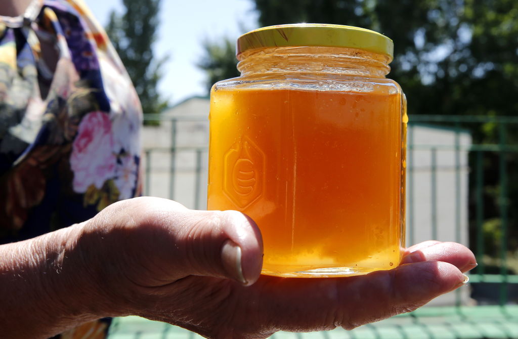 A jar of honey is held in someone's palm.