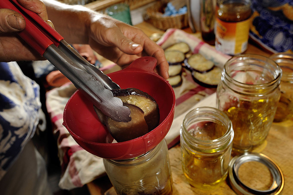 Someone uses tongs to ease pickled eggplant into a jar.
