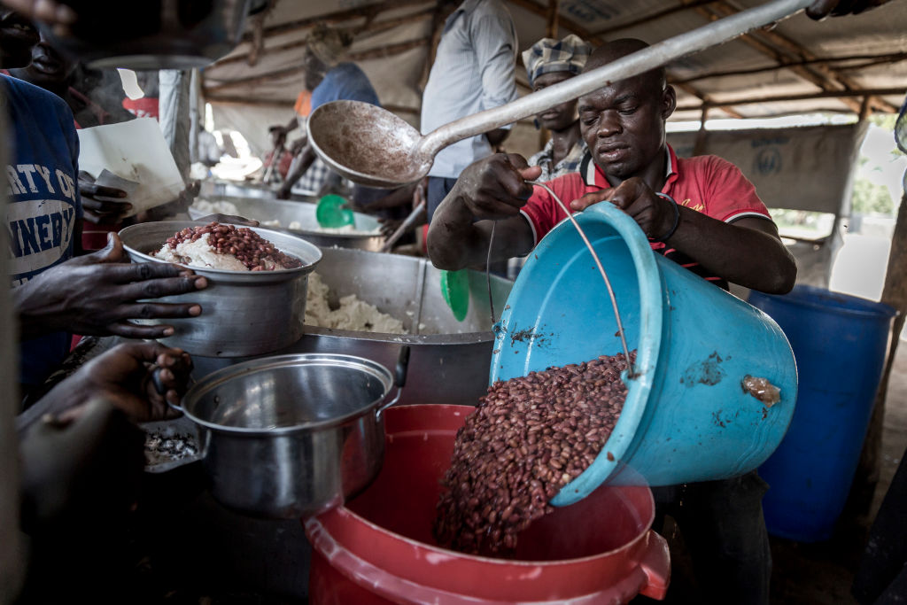 A man pours cooked beans out of a smaller bucket and into a larger one.