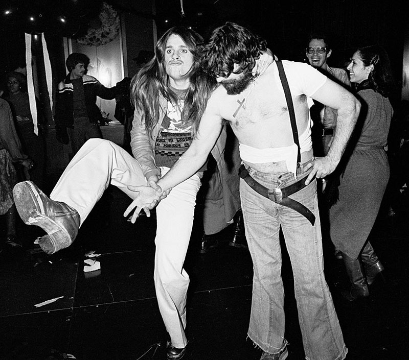 Ozzy Osbourne makes a duck face while kicking up one of his legs and gripping onto his band mate.