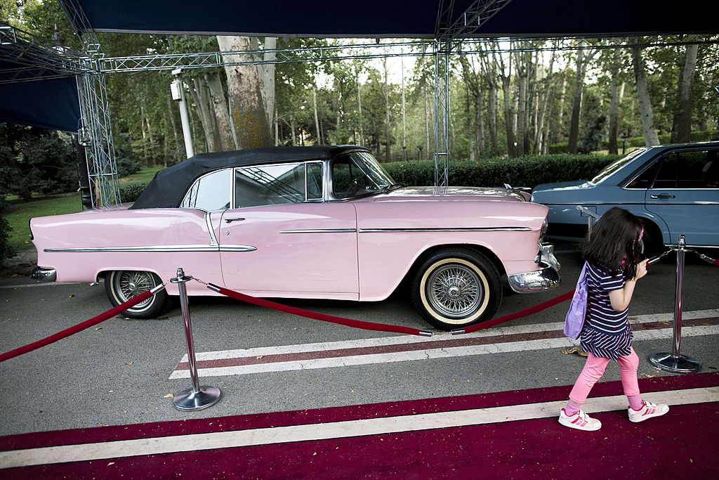 Pink Bel Air girl walks past a 1955 American Chevrolet