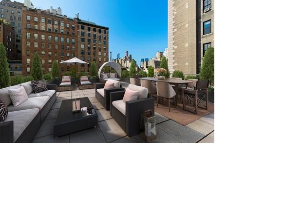 Lounge chairs, a couch, coffee table, two cushed chairs, and a long table reveal an outdoor living space with city views.