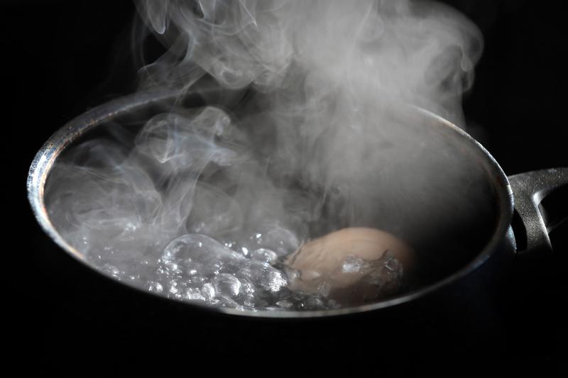 An egg lies in a pot on a hotplate in boiling water. 