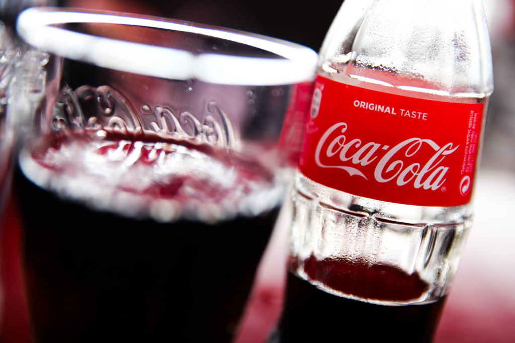 A bottle of Coca-Cola sits next to a glass