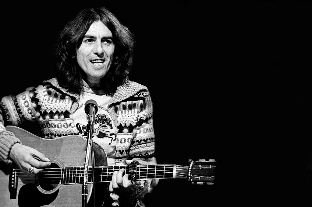 George Harrison playing guitar in a sweater 
