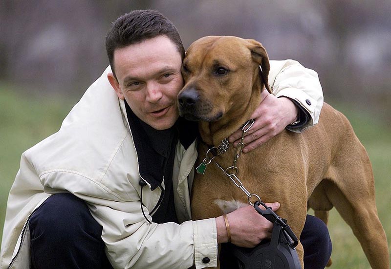 A man leans down to hold his Rhodesian Ridgeback.