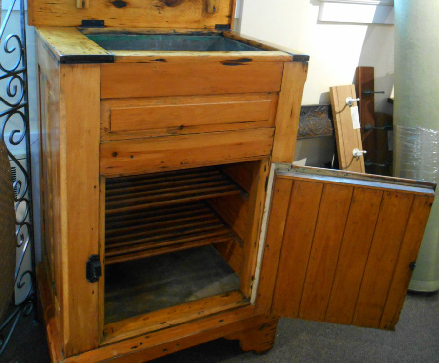 An antique wooden ice box is open.
