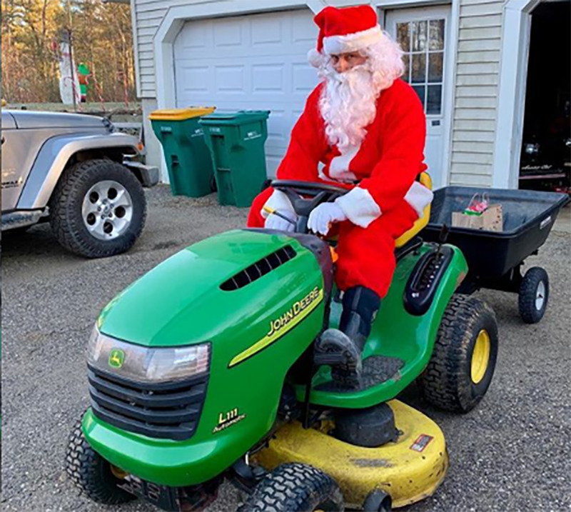 A man dressed up as Santa Claus sits on a tractor in the driveway.