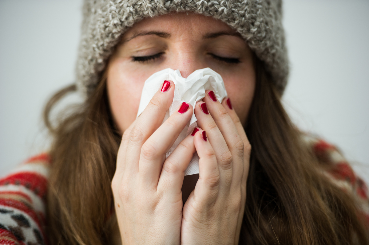 A young woman uses a tissue to blow her nose.
