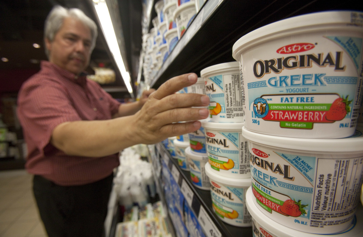 reaching for Greek yogurt - 165221762 Dairy manager stocks Greek yogurt at a grocery store.