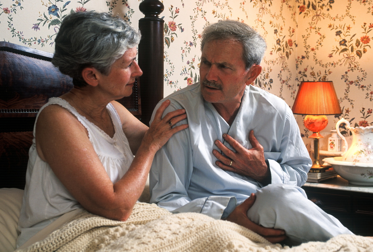 Senior man with chest pain is comforted by his concerned wife.