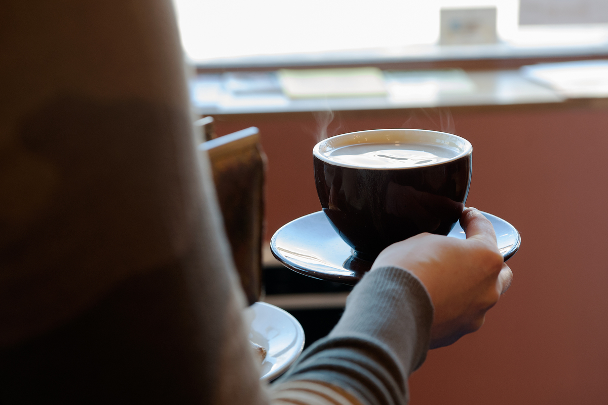 A customer carries a cup of coffee to her table at Colson Patisserie.