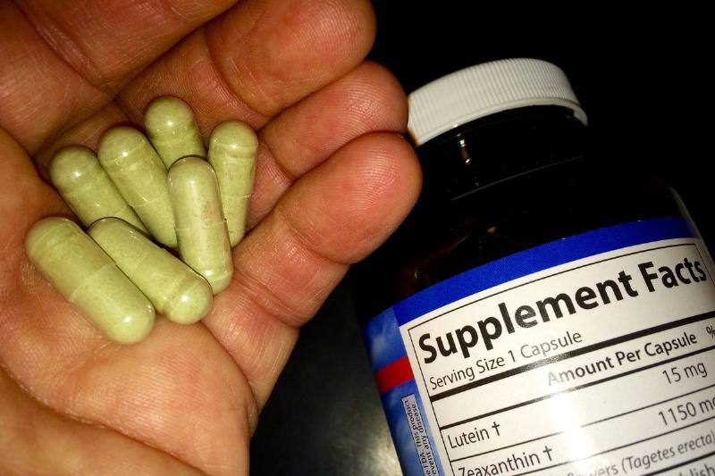herbal supplements - 537566727 A man holds marigold herbal supplement capsules with the bottle nearby.