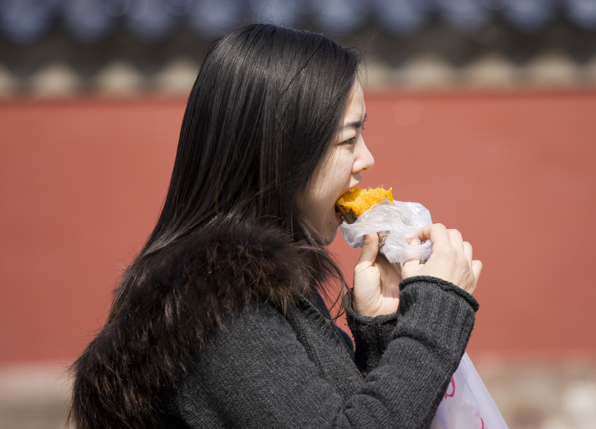 eating a sweet potato - 81749200 Girl eats a sweet potato at the Ming Dynasty Temple of Heaven, Beijing, China.