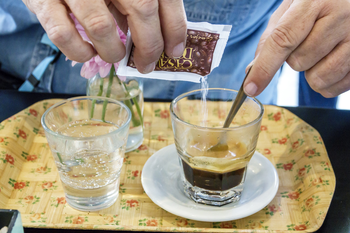 Person pours sugar into an espresso coffee.