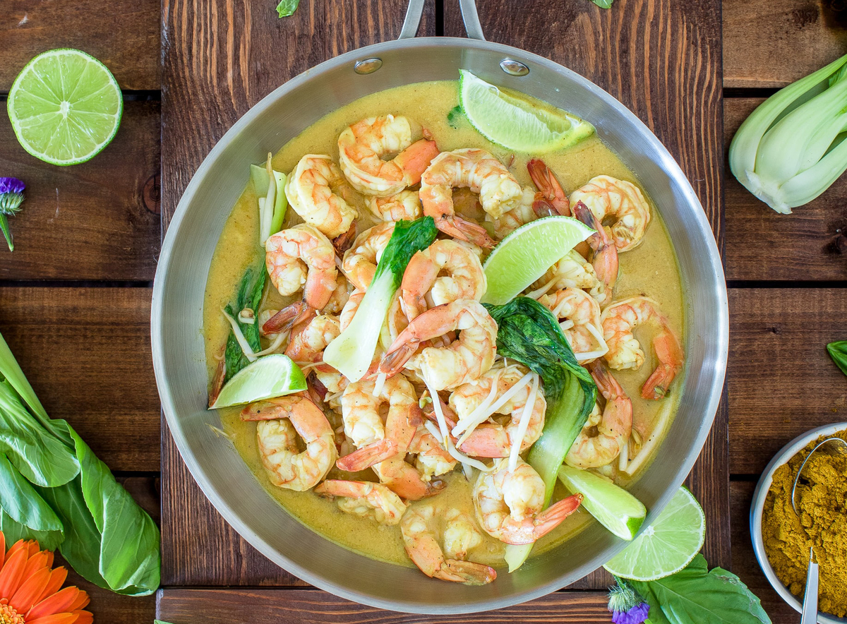 A pan of curry shrimp lies against a wooden table.