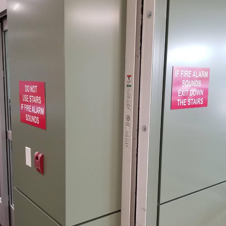 sign saying not to use stairs in fire, and another sign saying use stairs not elevator during fire