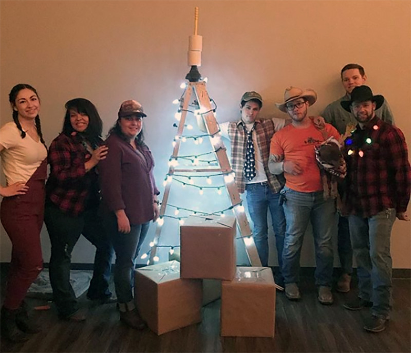 Friends pose next to a makeshift Christmas tree topped with a plunger.
