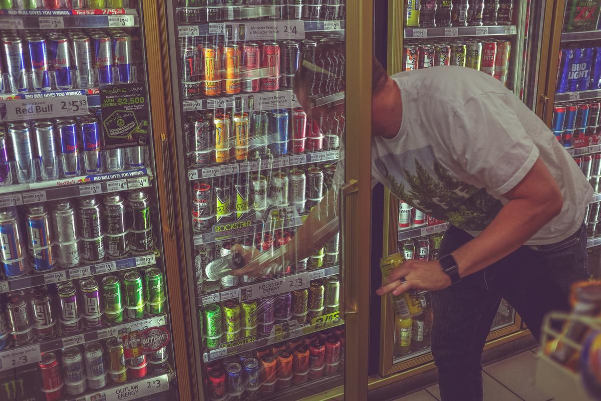 Man reaches into a gas station fridge to get an energy drink.