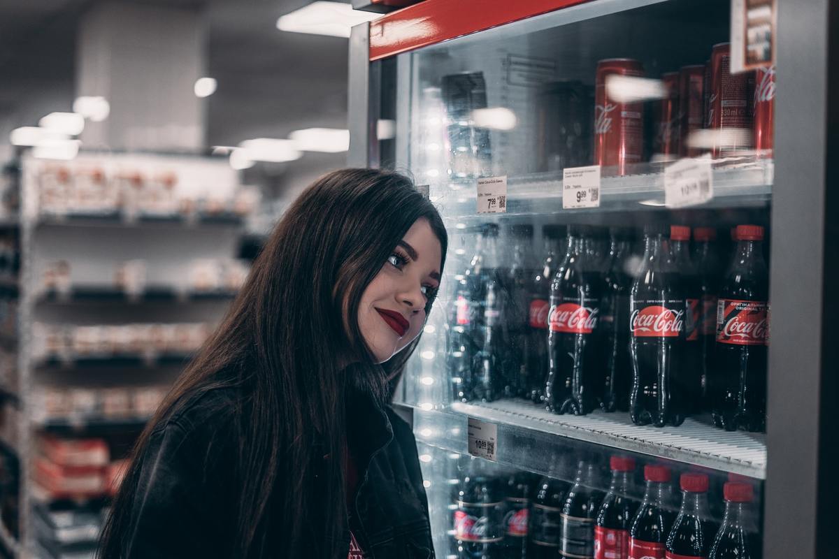 Woman looks at a fridge full of soda.
