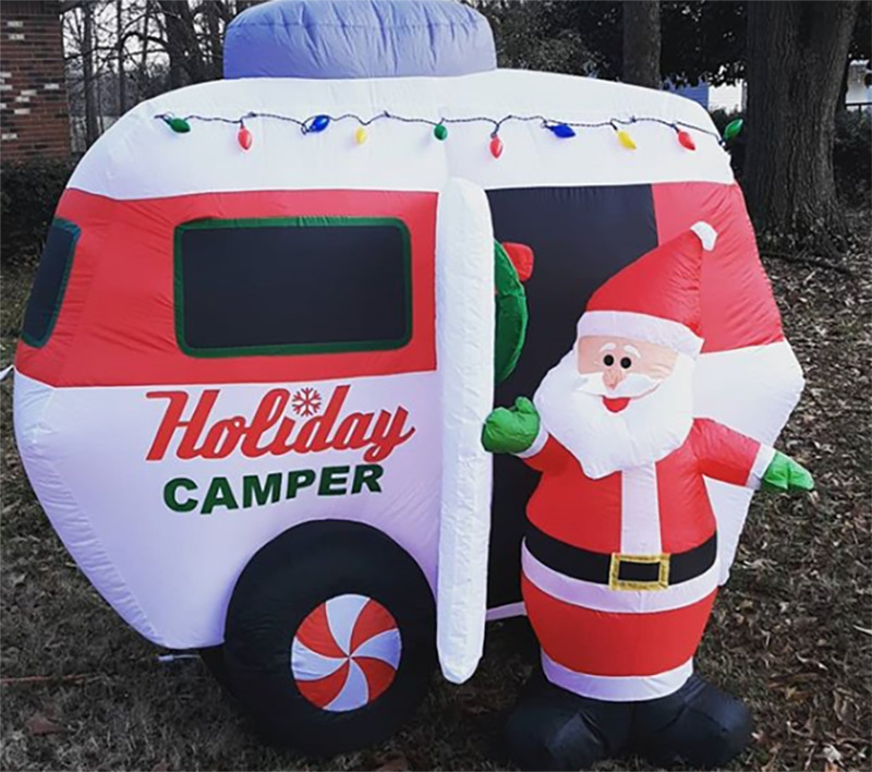 A blow up Santa Claus and camper sit in a front yard.