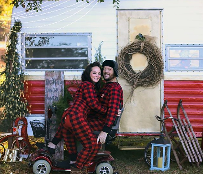 A couple in pajamas poses on a mobility chair in front of an RV.