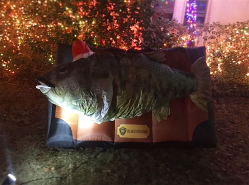 A blow up Billy the Big Mouth Bass is leaned up in a yard before Christmas lights.