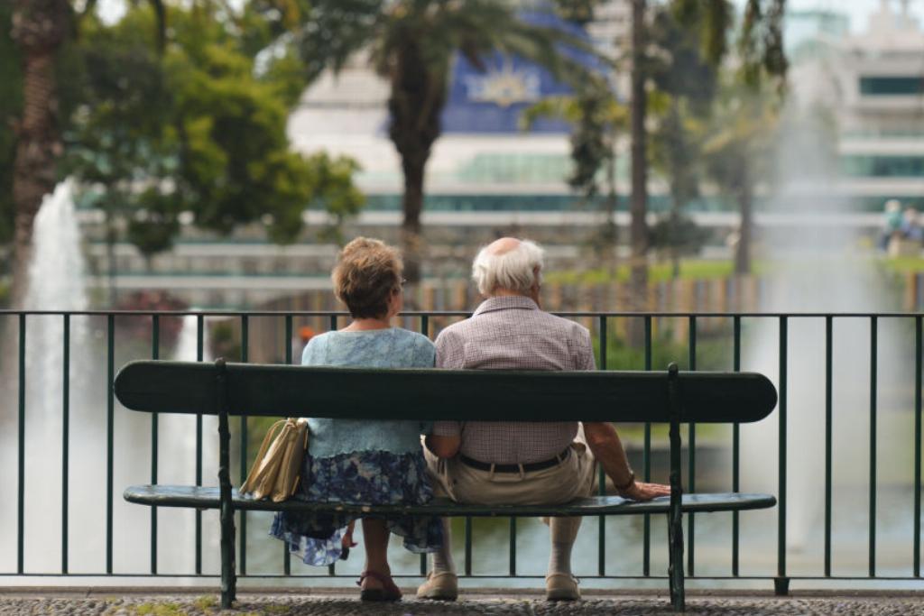 elderly-couple A elderly couple sits on a bench near a lake.