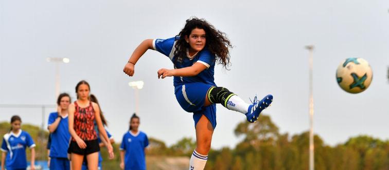 A girl kicks a soccer ball across the field.