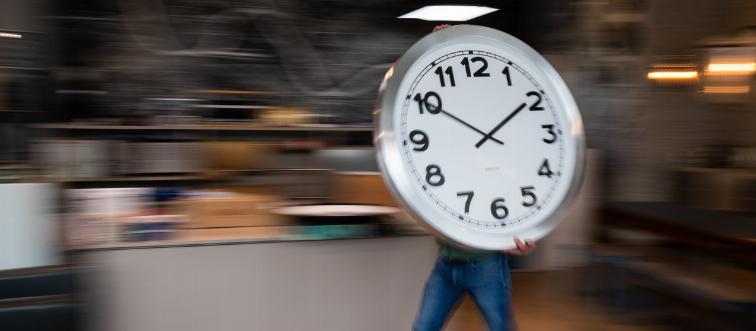 A man carries a large clock across a room.