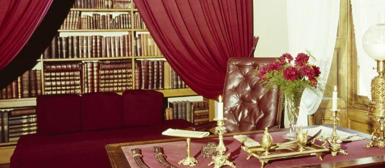 A room contains a red desk, sofa, and curtains.