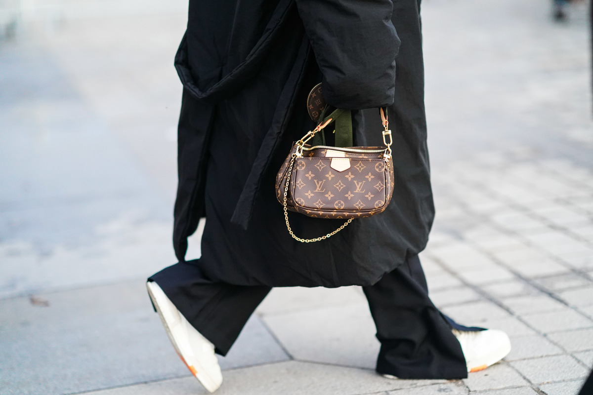 small purse - 1178851495 A person wearing an oversized coat carries a small Louis Vuitton bag.