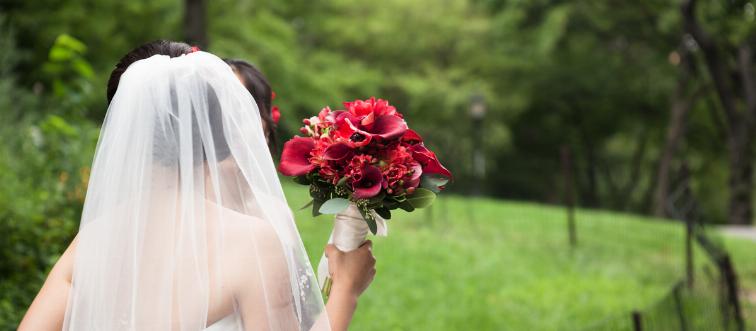 A bride wears a veil and holds a red floral bouquet.