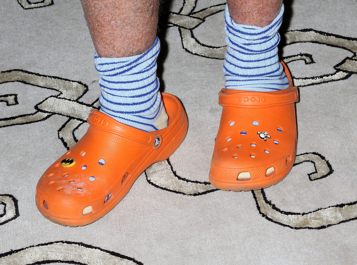 crocs - 614601402 A man wears orange crocs with skull and Batman decorations.