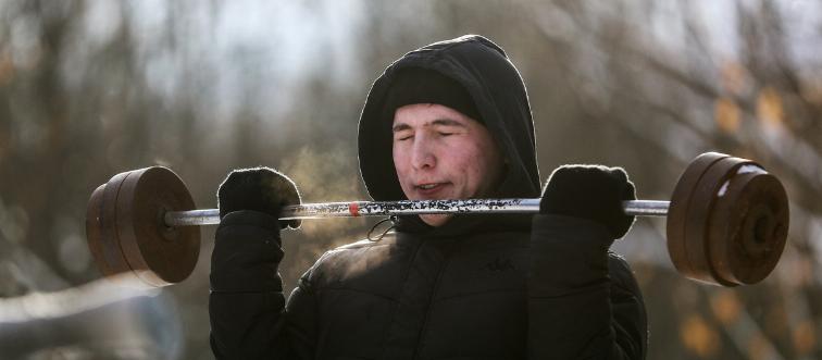 A man lifts a barbell outside in the snow in Russia.
