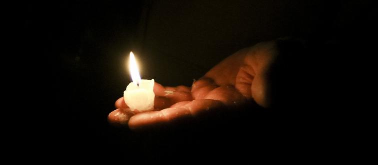 A person holds a small candle in the dark.
