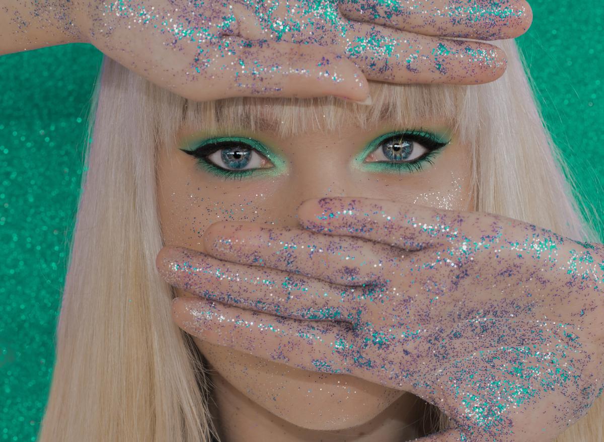 glitter everywhere A woman has blue and purple glitter all over her hands and face.