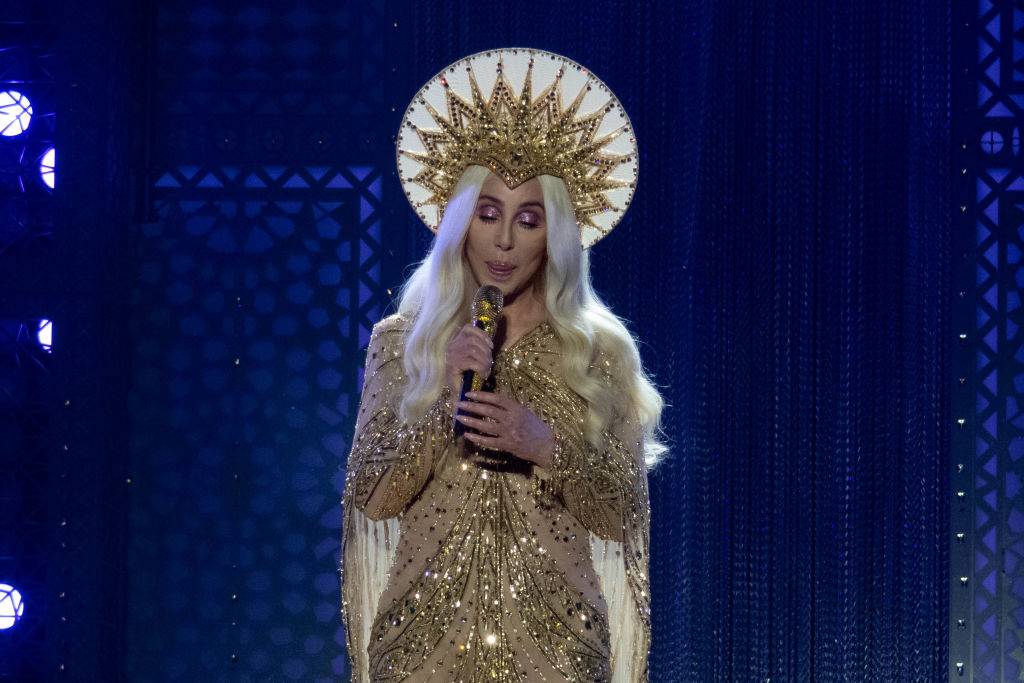 Cher wears a glittering, gold outfit and matching headpiece while performing live.