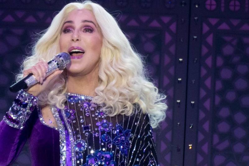 Cher boasts blonde hair and a purple outfit while singing live.