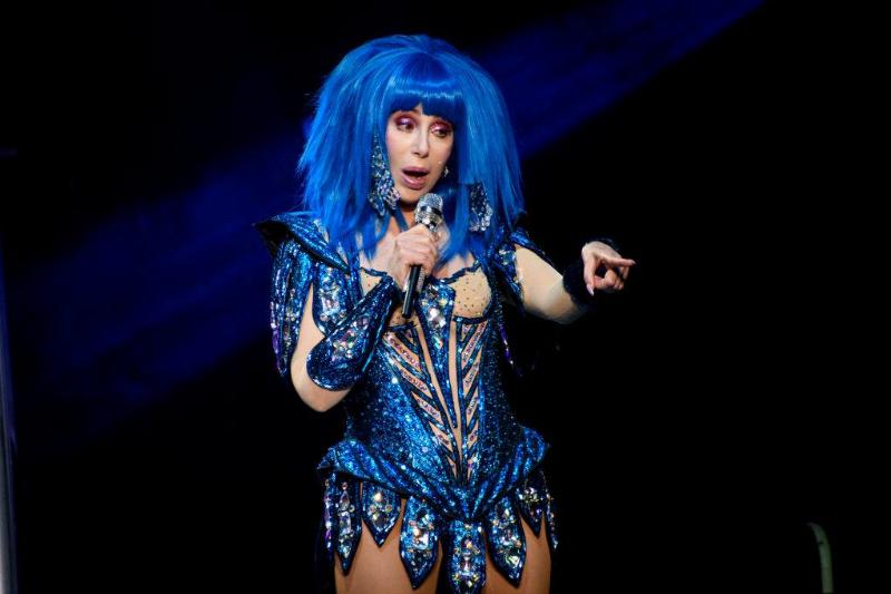 Cher wears a print blue outfit and matching wig while performing onstage.