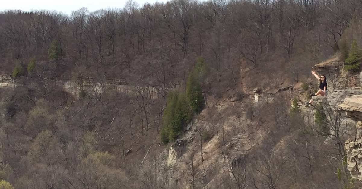 A woman poses on a cliff with her hand in the air.