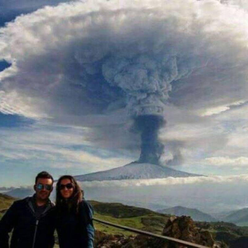 couple standing in front of an erupting volcano 