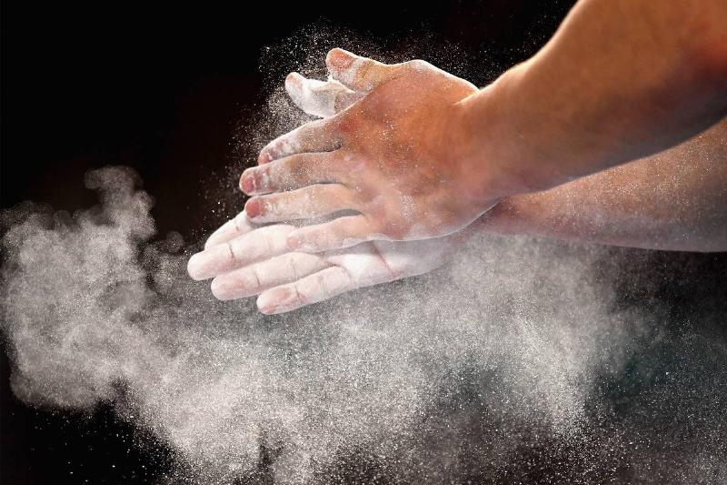 A gymnast rubs chalk powder on his hands.